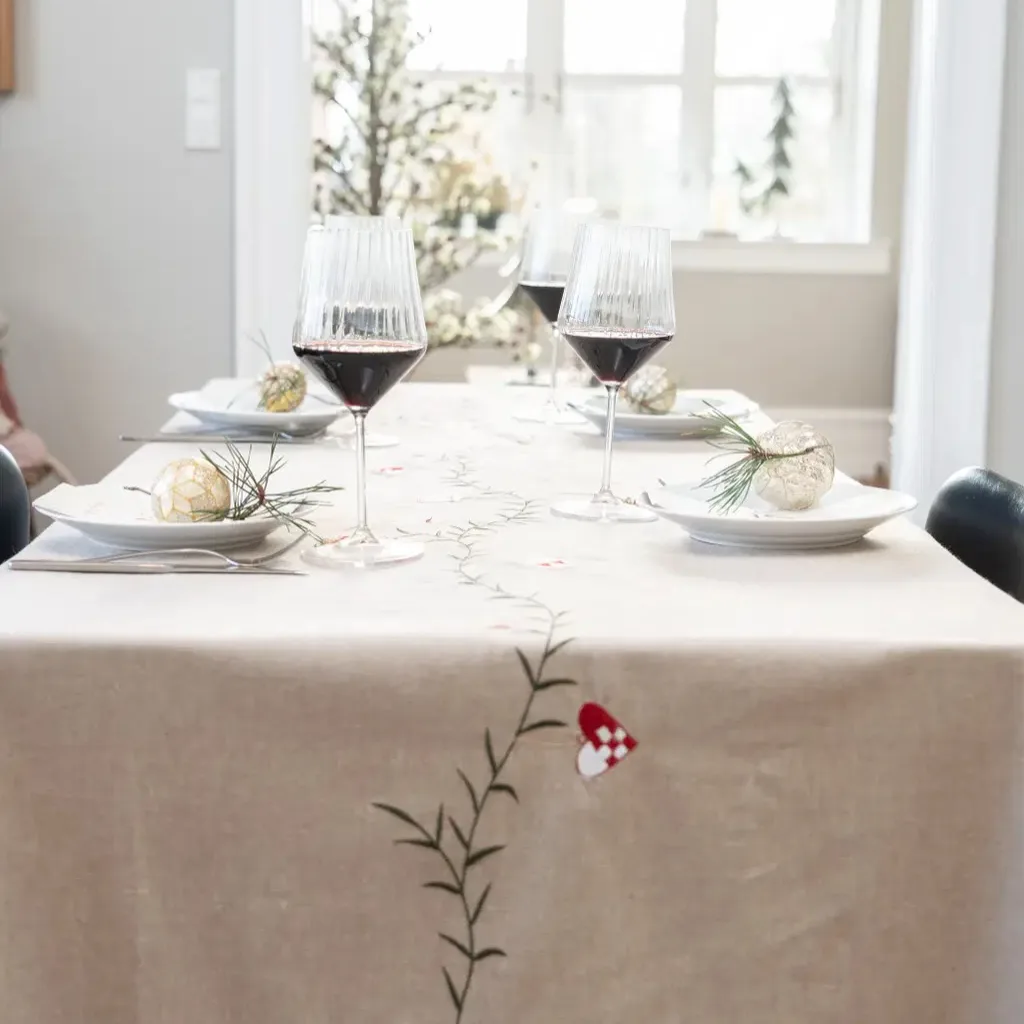 Dækket julebord med broderet juledug i hør, vinglas og julekugler